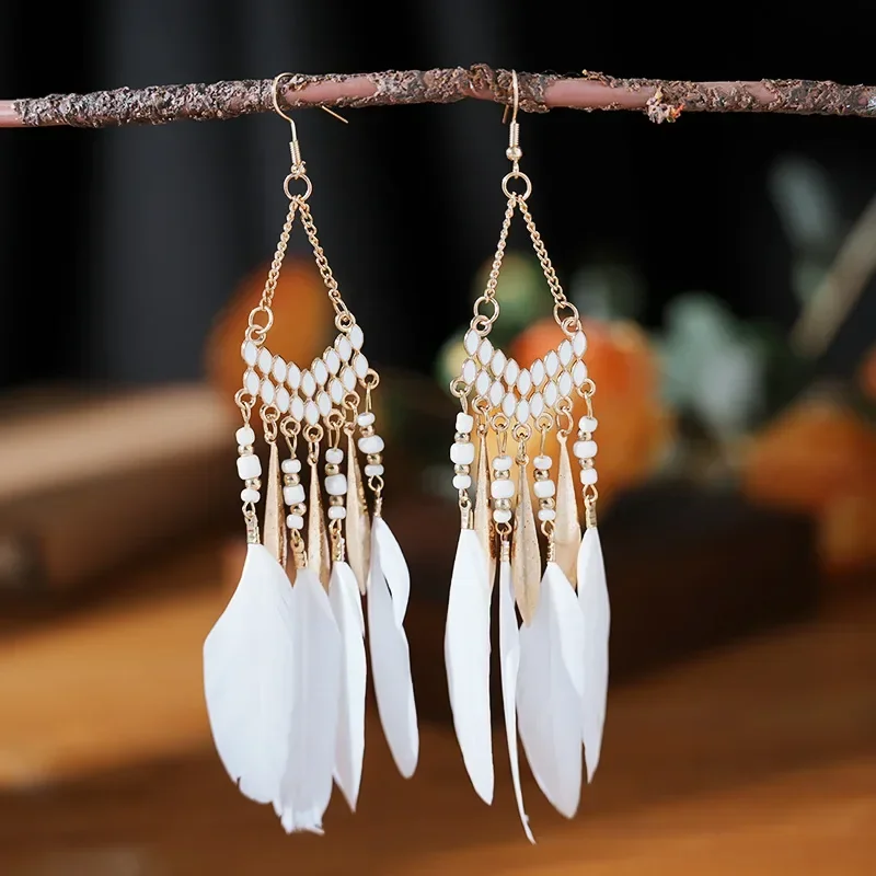 A pair of gold-toned chandelier earrings featuring white beads, metallic teardrops, and white plumes hanging from a branch.