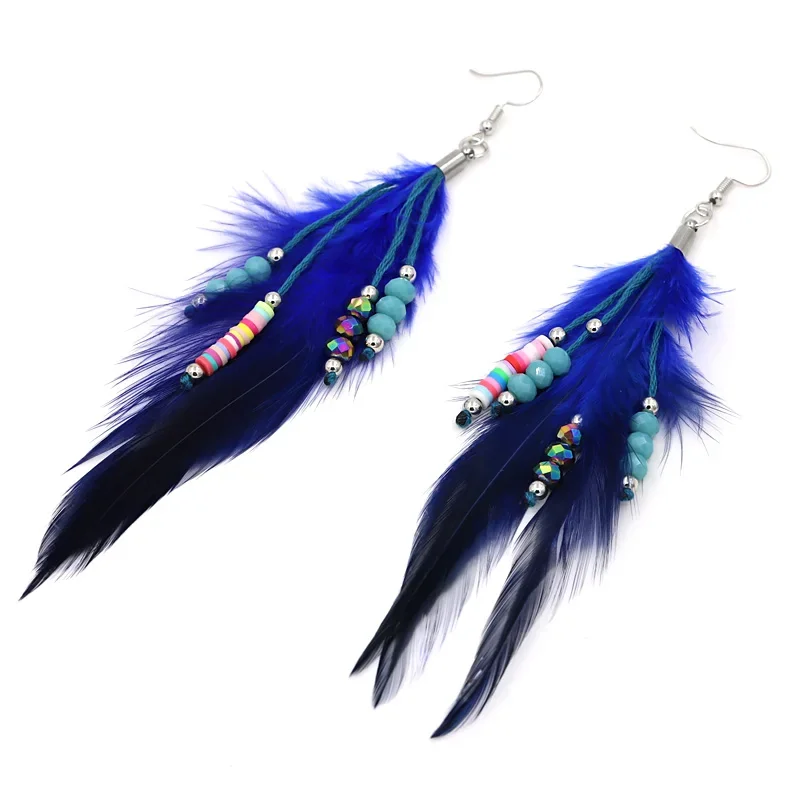 Two long, vibrant blue feather drop earrings with hanging bead strands laid out on a white surface.
