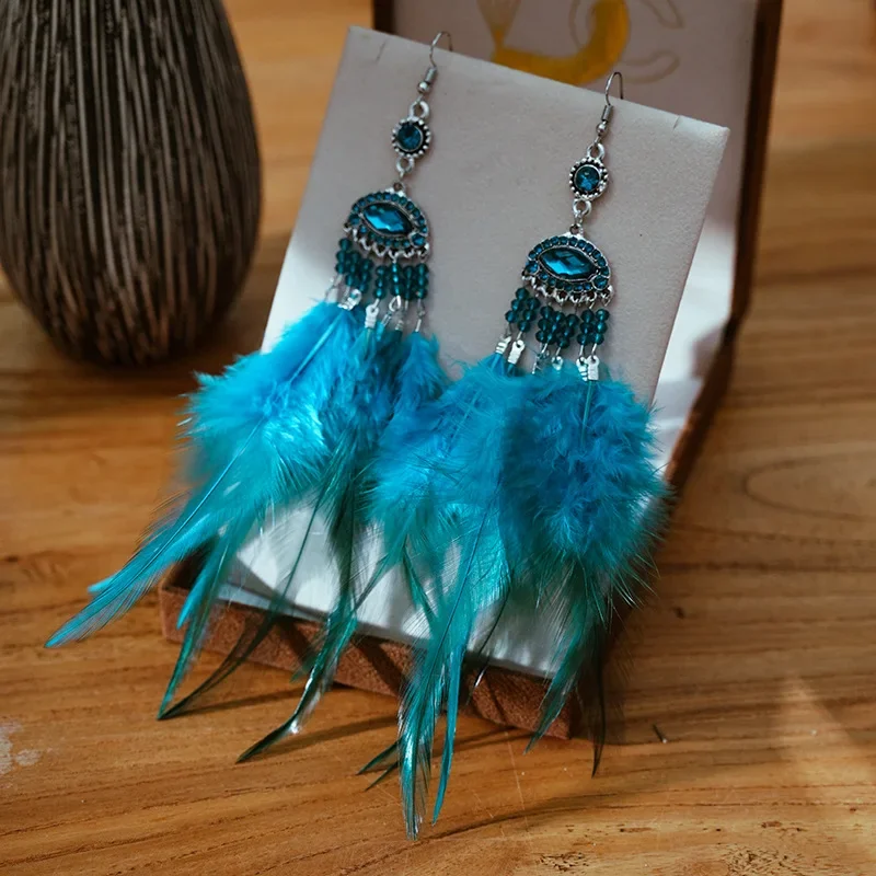 Blue chandelier earrings with faceted stones, beaded strands, and bright blue feathers displayed on a jewelry stand.