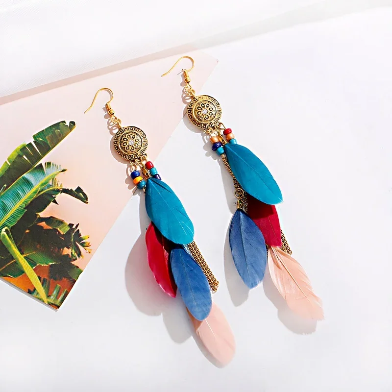 Long drop earrings featuring a gold-toned etched medallion top, multi-colored feathers, and fine metallic chains hanging below.