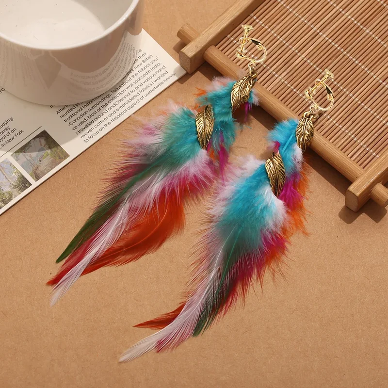 A pair of clip-on earrings with vibrant multi-colored plumes ranging from teal to orange, accented by small gold-tone leaf charms.