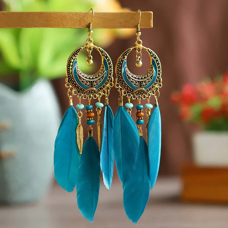 Blue crescent-shaped metal earrings with hanging beads, metal leaves, and blue feathers.