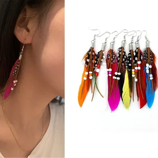 A woman wears a long, slender feather drop earring with brown cords, spotted feathers, and white beads.