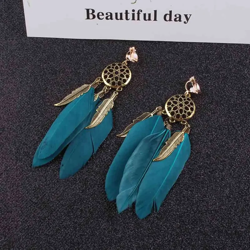 A pair of clip-on earrings featuring a gold-toned openwork circular medallion with several dark feathers dangling below.
