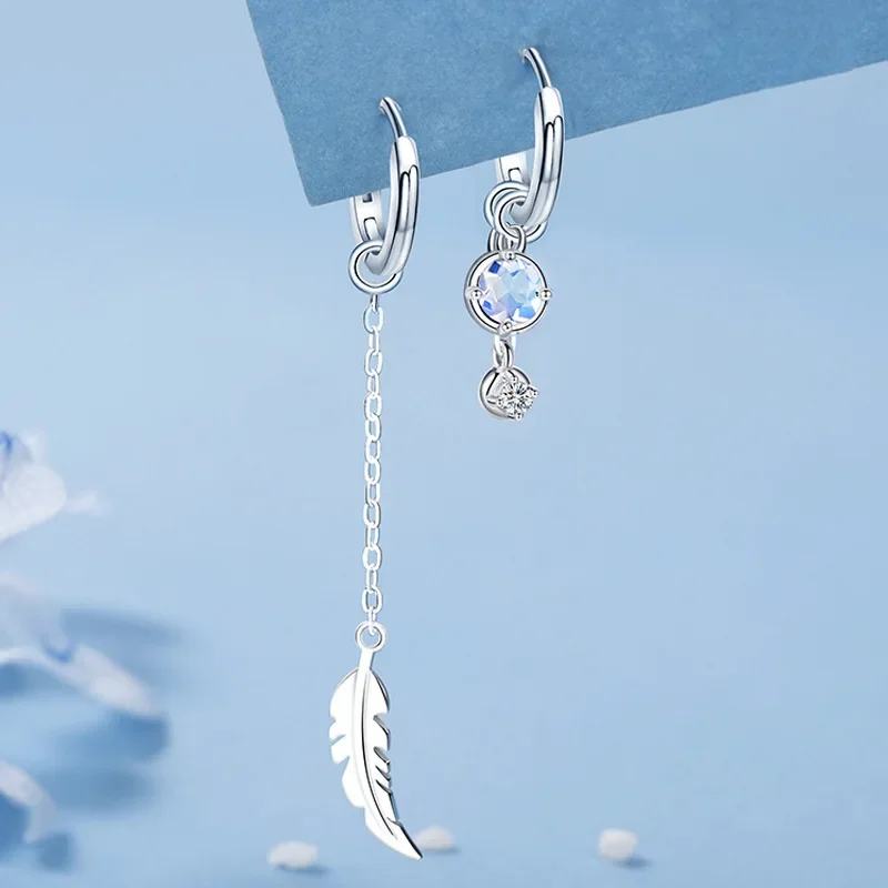 Asymmetric silver-tone earrings with one side featuring a long chain and feather charm, and the other featuring stone studs.