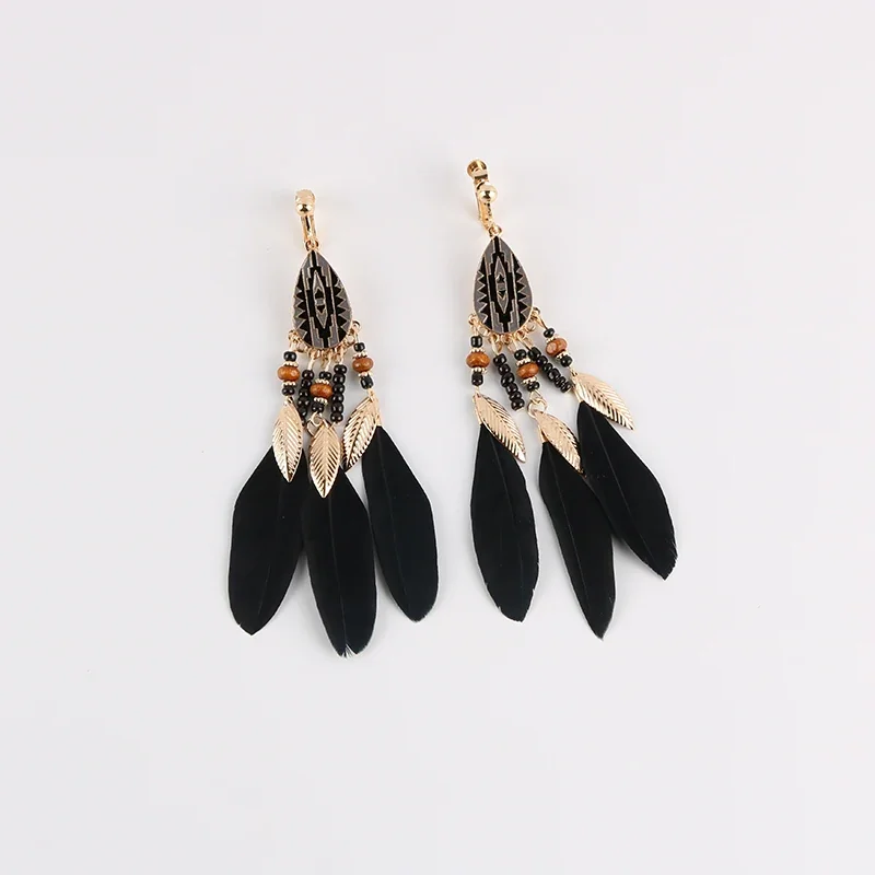 A pair of clip-on earrings featuring a teardrop metal component with geometric patterns, beads, and black feathers.