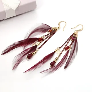 A pair of deep red feather earrings with hanging chains, beads, and small gold-toned leaf charms.