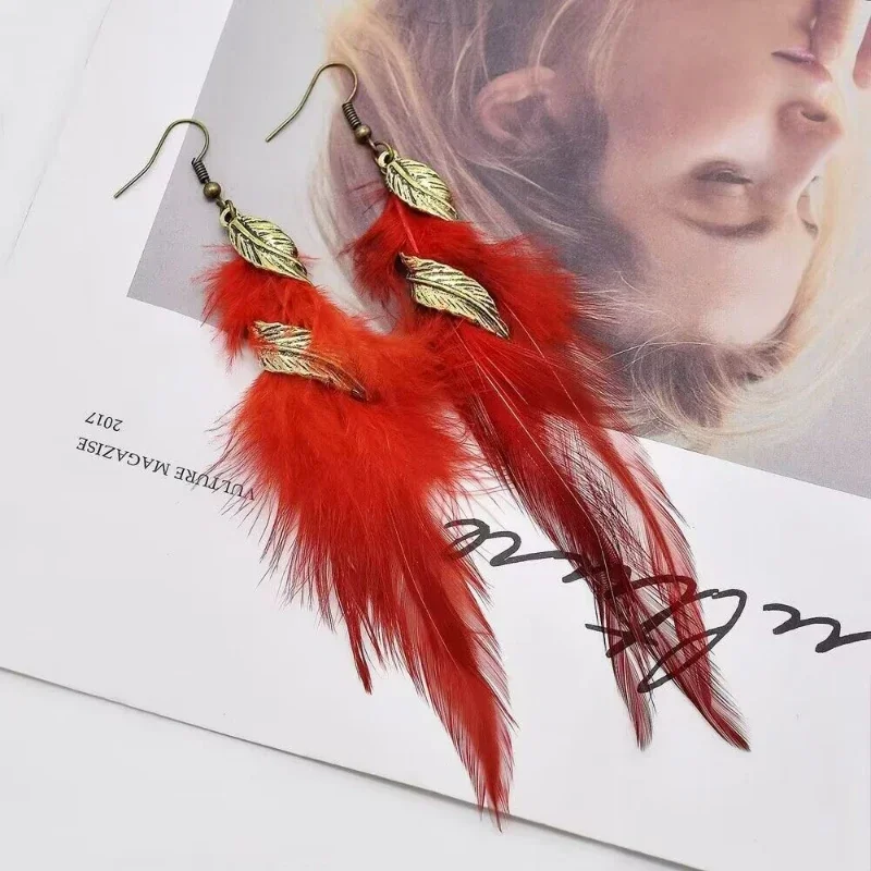 A pair of drop earrings featuring soft red plumes and metallic leaf-shaped charms hanging from a hook closure.