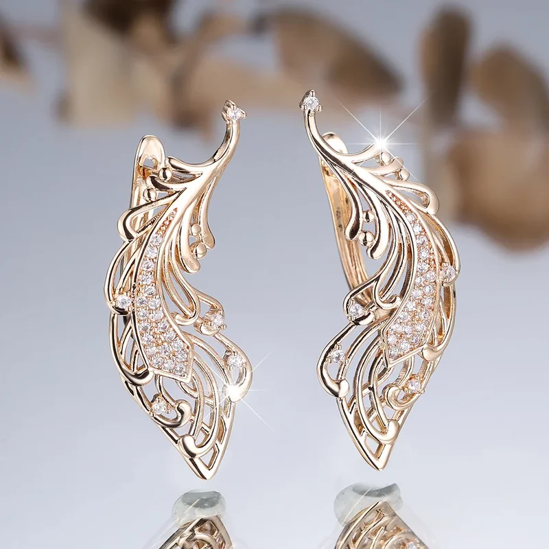 A pair of gold-toned wing-shaped earrings with intricate filigree and small sparkling accents.