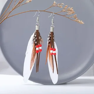 A pair of long feather drop earrings with white feather shapes, narrow patterned strands, and small red bead accents.
