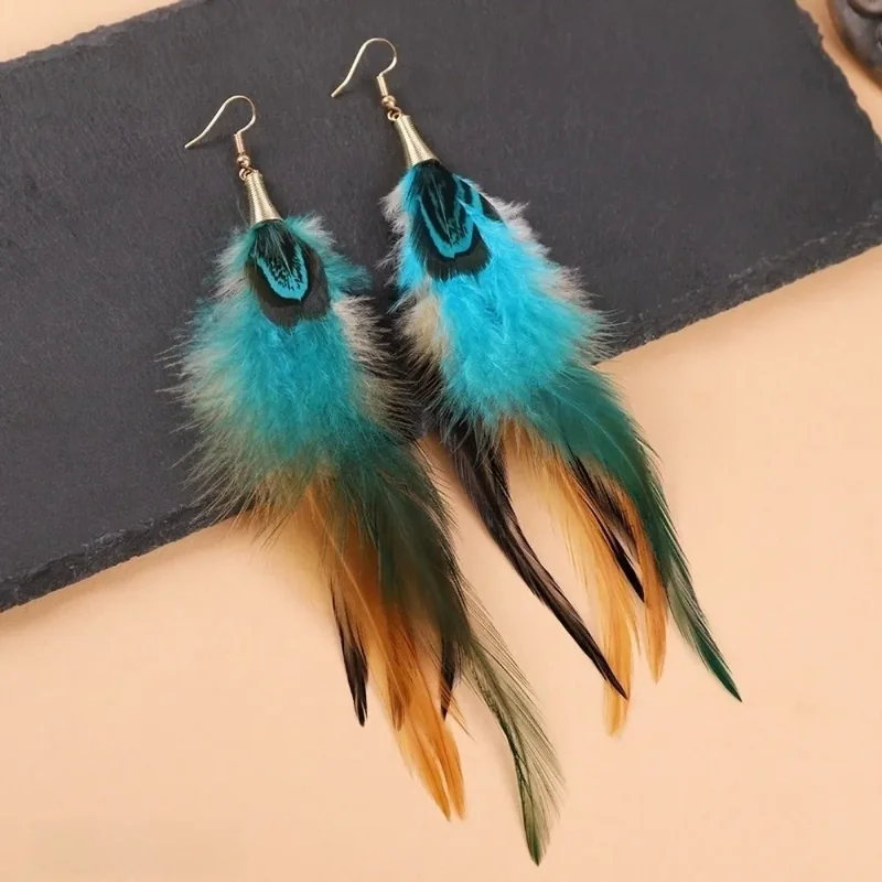 Blue and tan plume drop earrings with patterned eye-like upper accents, wispy clusters, and longer narrow feather strands.