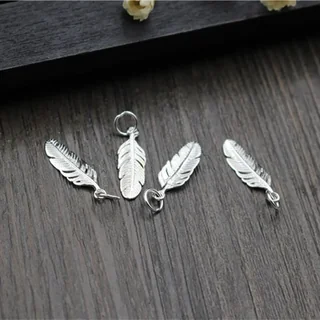 Four silver-toned feather-shaped jewelry charm components with small top loops arranged on a dark wooden surface.