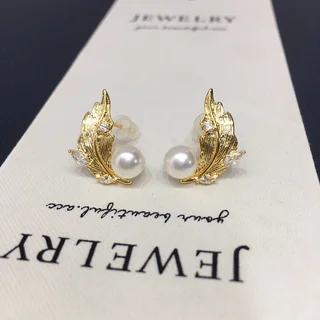 A pair of gold-toned wing-shaped stud earrings featuring a smooth round accent and small clear highlights on a jewelry display card.
