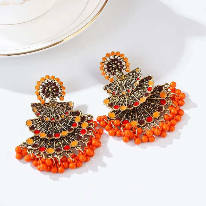 A pair of orange and dark red fan-shaped metal earrings with a bottom fringe of matching orange beads.