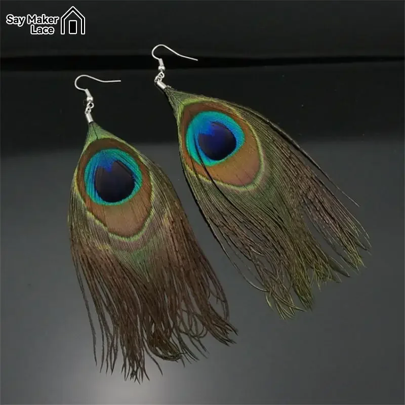 Two peacock feather drop earrings with visible eye patterns and long, dark plumes against a black background.