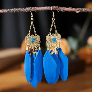 Two drop earrings featuring ornate stamped metal discs, central stone accents, hanging chains, and bright blue or red plumes.