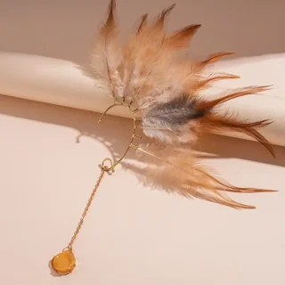 A gold-toned ear cuff featuring brown feathers and a dangling chain with a round amber charm.