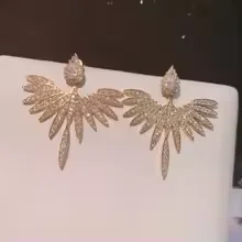 A pair of shimmering, wing-shaped stud earrings displayed on a white stand.