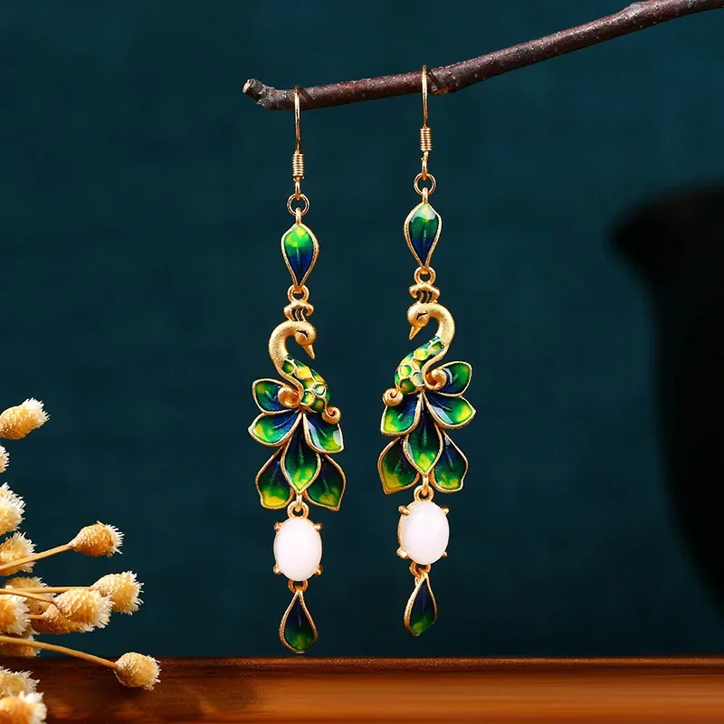 A pair of gold-toned earrings featuring an enameled peacock design and a white stone drop.
