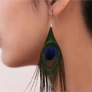A close-up of a long, iridescent peacock feather drop earring hanging against a person's neck.