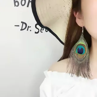 A single peacock plume drop earring worn on a person, showing the vibrant blue and green eye detail.