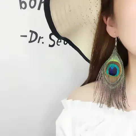A single peacock plume drop earring worn on a person, showing the vibrant blue and green eye detail.
