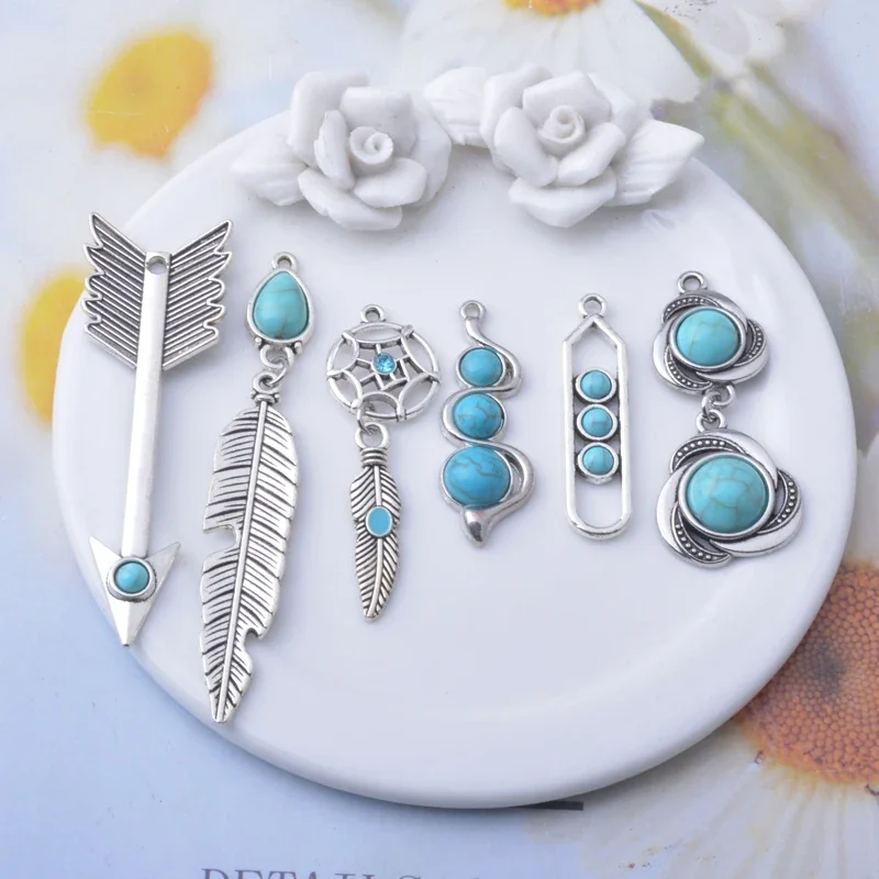 An assortment of silver-toned jewelry charm components with feather-like shapes, pointed motifs, and blue rounded decorative accents.