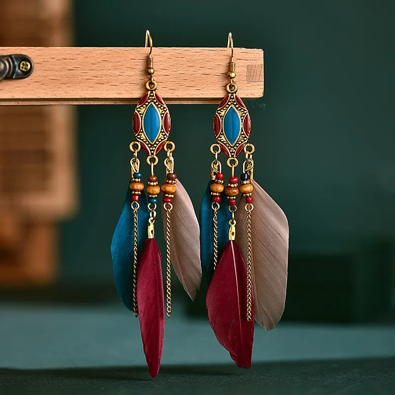 A pair of drop earrings featuring geometric metal frames with blue accents, hanging chains, and layered plumes.