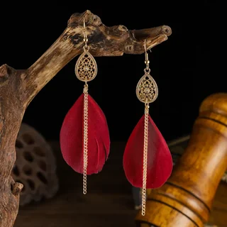 Two gold-tone teardrop earrings with central chains and red feathers hanging from a branch.