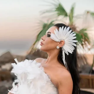 A model wearing a large white feather fan arranged around the ear in a sweeping wing-like shape.