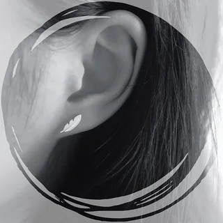A close-up of a silver-toned feather-shaped stud earring worn on an earlobe, showing fine etching and a curved shape.