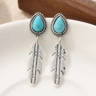 A pair of drop earrings with a turquoise-colored teardrop stone and a hanging silver-toned metal feather.